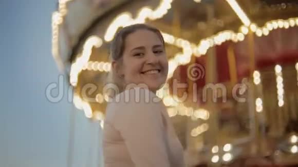 一幅美丽的微笑女子站在游乐园的明亮旋转木马旁的画像视频的预览图