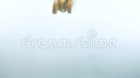 猕猴桃片在白色背景下慢慢落入清澈的水中视频的预览图