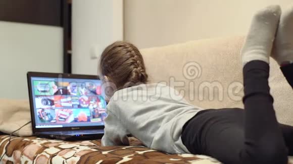 有趣的小女孩坐在沙发上用笔记本电脑和微笑视频的预览图