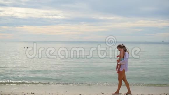 阳光明媚的一天带着孩子的女孩在海滩上散步和玩耍视频的预览图