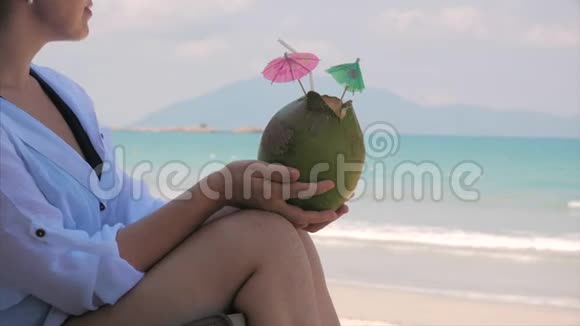 一个欧洲美丽可爱的黑发年轻女人或一个快乐的女孩的肖像在阳光下喝椰子在风中喝一杯视频的预览图