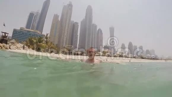 这个男孩沐浴在大海中在迪拜摩天大楼的背景下喷水慢速射击视频的预览图