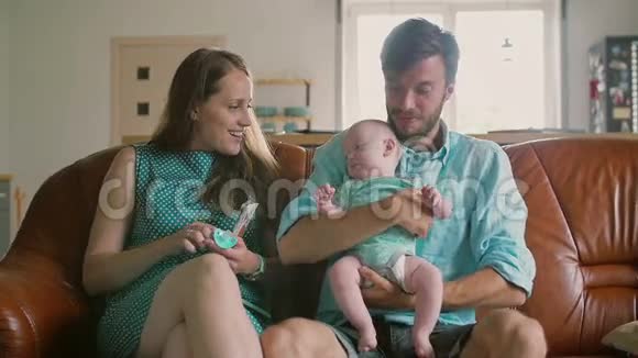 四口之家正坐在沙发上父亲抱着刚出生的儿子女儿高兴地在他们身边跳跃慢节奏视频的预览图