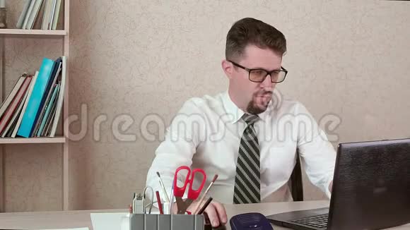 一个男人是一个办公室工作人员胡子和眼镜在笔记本电脑上工作视频的预览图