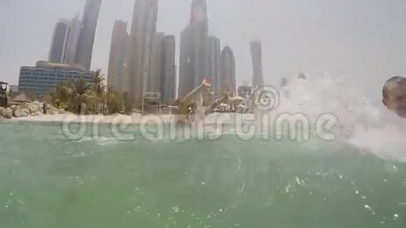男孩和女孩沐浴在大海中在迪拜摩天大楼的背景下喷水慢动作视频的预览图