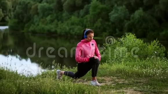 一个穿着粉色夹克的女孩正在准备跑步热身通过电话用耳机听音乐视频的预览图