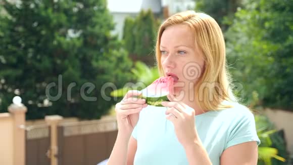 年轻漂亮的金发女人在户外对着天空和树木吃西瓜4k慢动作视频的预览图