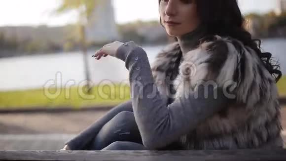 坐在河岸上的漂亮女孩模糊了城市的背景柔和的秋光特写视频的预览图