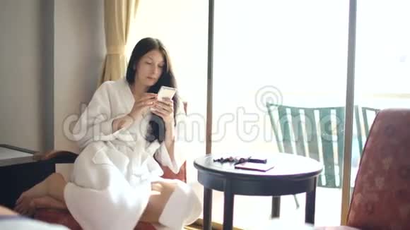 酒店客房内坐在椅子上为自己化妆的快乐女人浴袍视频的预览图