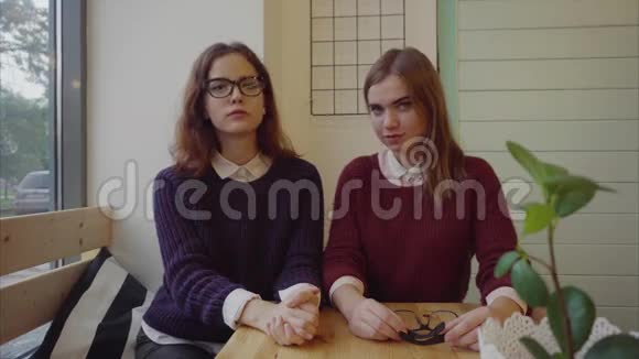 两个漂亮的女生戴着眼镜坐在咖啡馆的桌子旁看着镜头视频的预览图