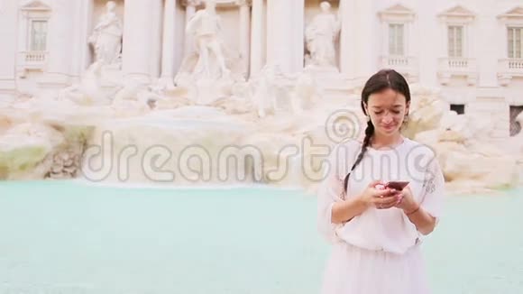 在欧洲著名的FontanadiTrevi附近的城市里一个在户外温暖的日子里带着智能手机的年轻女子视频的预览图