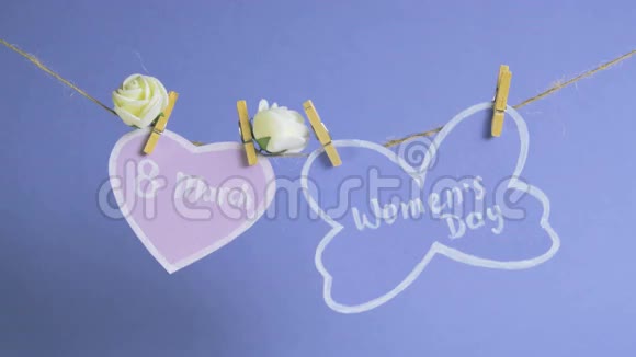 妇女节快乐妇女节纸上挂在一根绳子上靠近粉红色的纸心蓝色的背景上有花视频的预览图