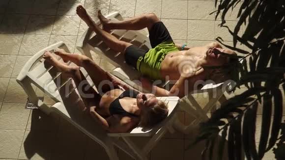 在游泳池附近晒日光浴美丽的男人和女人躺在日光浴床上日落日出视频的预览图