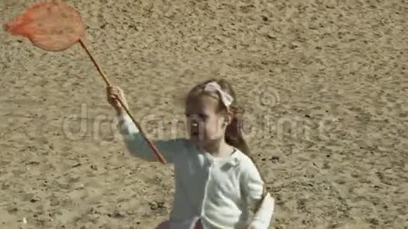 在一个阳光明媚的夏日一个可爱的小女孩正在河边的小巷里用绿色的铲子网捉昆虫视频的预览图