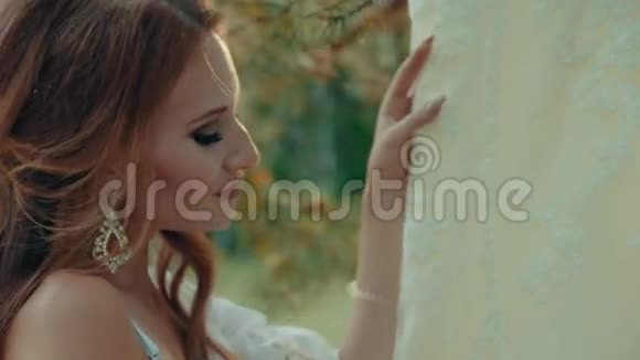 穿着内衣的女人抚摸着挂在松枝上的婚纱视频的预览图