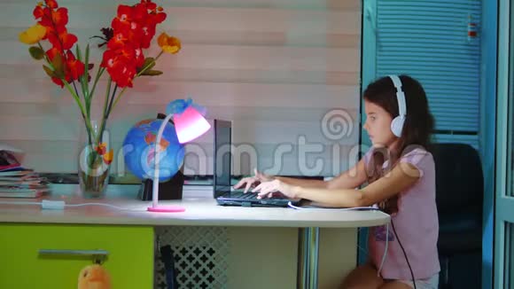 小女孩带着耳机在笔记本电脑上玩网络游戏电脑上的小女孩在社交媒体上留言视频的预览图