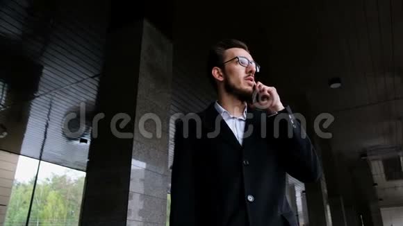 一位穿着经典服装戴眼镜的严肃经理站在办公室旁边的街道上接电话视频的预览图