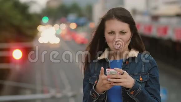开朗快乐微笑的漂亮女人用智能手机站在桥上玩得开心摆姿势看着相机4K视频的预览图