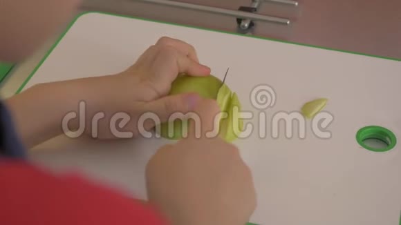 男孩正在用白色切割板上的厨房刀切苹果男孩在厨房桌子上切生蔬菜视频的预览图