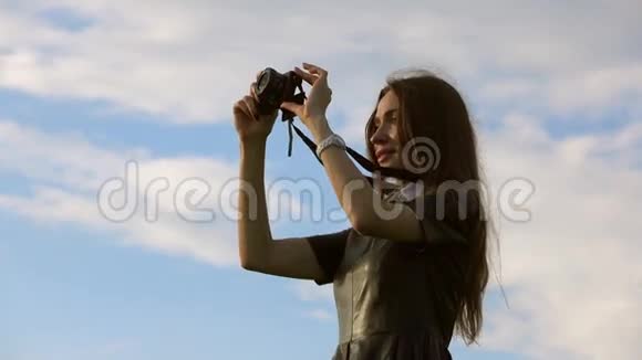 美丽的黑发女孩穿着黑色连衣裙对着天空用她的紧凑型相机拍照4K视频视频的预览图