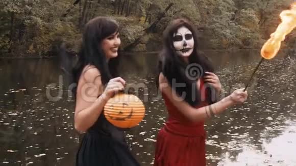年轻的万圣节女朋友穿着黑色和红色的女巫礼服在森林公园里玩着传统的秋季假期视频的预览图