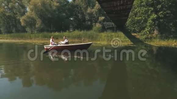 新娘和新郎坐在一艘白色的小船上从树上漂出来往湖里漂视频的预览图