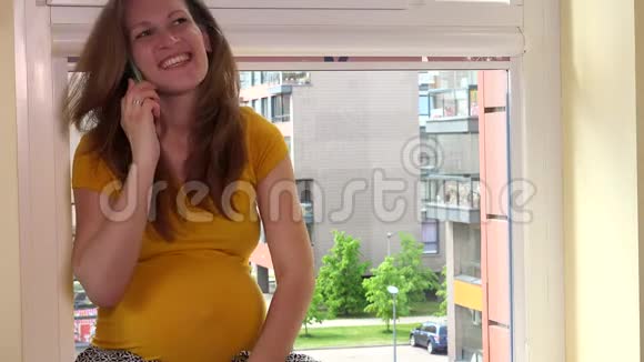 幸福微笑的孕妇坐在窗台上打电话视频的预览图