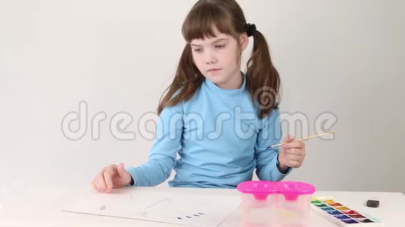 蓝色水彩画中的微笑女孩在白色房间的桌子上画蝴蝶视频的预览图