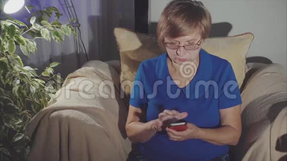坐在扶手椅上的一位在家使用智能手机的老年妇女视频的预览图