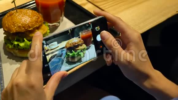 女孩在一家咖啡馆里的智能手机上拍了一张汉堡和番茄汁的照片视频的预览图
