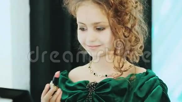 穿着绿色连衣裙的小女士坐在镜子和口红前视频的预览图