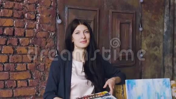 年轻女艺术家的慢镜头肖像站在完成的图片附近微笑进入相机视频的预览图