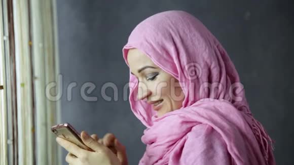 漂亮的穆斯林女人在窗前打电话视频的预览图