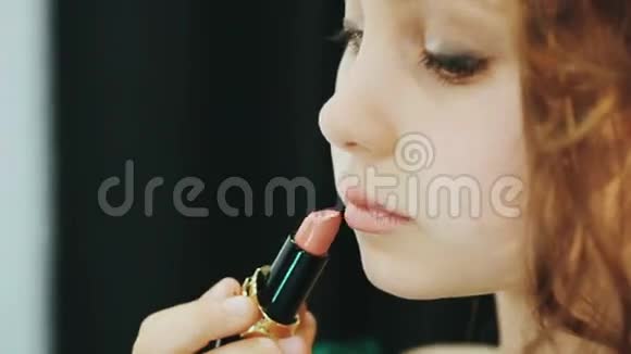 穿着绿色连衣裙的小女士坐在镜子和口红前视频的预览图