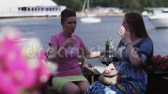 穿着粉红色衬衫的女孩和年轻的孕妇说话河边的露台电话视频的预览图