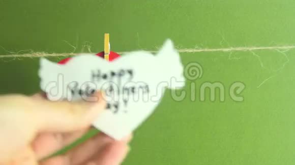 妇女节快乐双手固定一个白色的纸心翅膀在一根绳子上绿色背景上有一个衣架视频的预览图