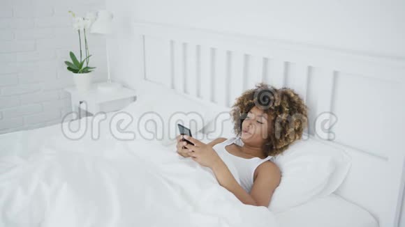 微笑的女人在床上用电话放松视频的预览图