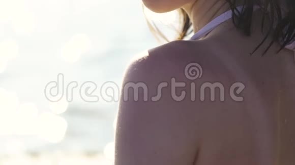 美丽的女孩在沙滩上为身体从瓶子里涂抹防晒霜视频的预览图