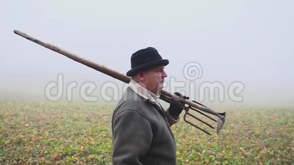 戴着帽子的老农在春田里拿着一把泥泞的锄头和鹳体力劳动福克视频的预览图
