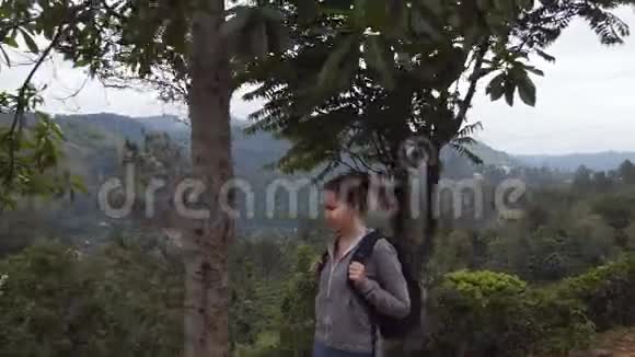 女徒步旅行者沿着热带山道年轻的女游客背着背包在山上漫步视频的预览图