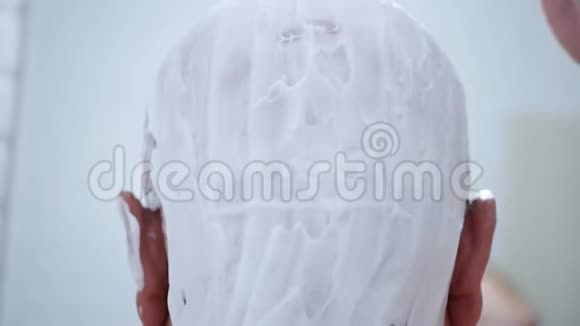 头上有白色泡沫的人用剃刀刮头发视频的预览图