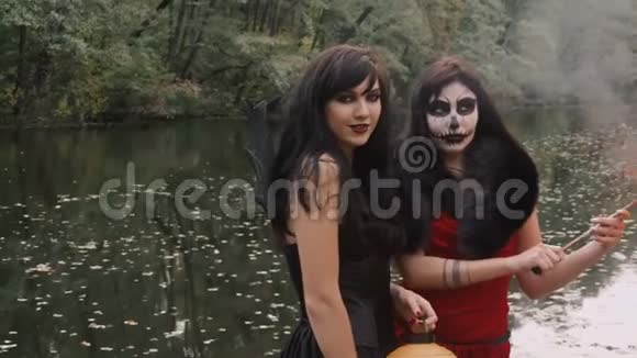 年轻的万圣节女朋友穿着黑色和红色的女巫礼服在森林公园里玩着传统的秋季假期视频的预览图