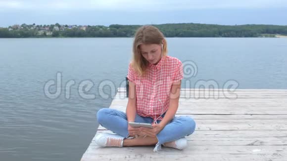 白种人女性坐在湖边看平板电脑视频的预览图