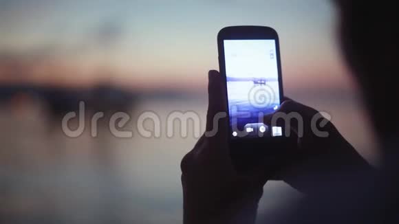 在智能手机上的男性手交谈照片剪影与美丽的日落与船1920x1080视频的预览图