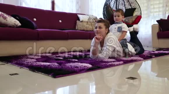 一位年轻的母亲和她的小儿子躺在客厅的地板上看电视视频的预览图