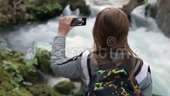 一个年轻女孩背着背站着的特写镜头拍摄了智能手机山瀑布视频的预览图