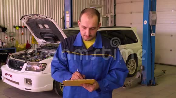 汽车机械师在汽车背景下用蓝色工作服填写文件视频的预览图