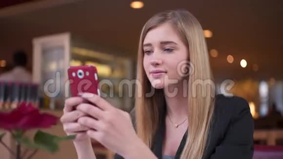 穿着黑色夹克的年轻金发女郎坐在咖啡馆A商店里她专注于和她的朋友发短信视频的预览图