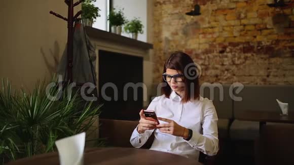 在咖啡店休息时带着美丽微笑在手机上阅读好消息的迷人女人快乐的高加索女性视频的预览图