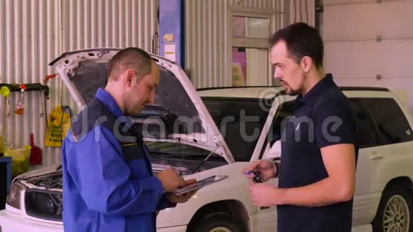 汽车修理工在车库里和车主一起测试汽车时使用小工具视频的预览图